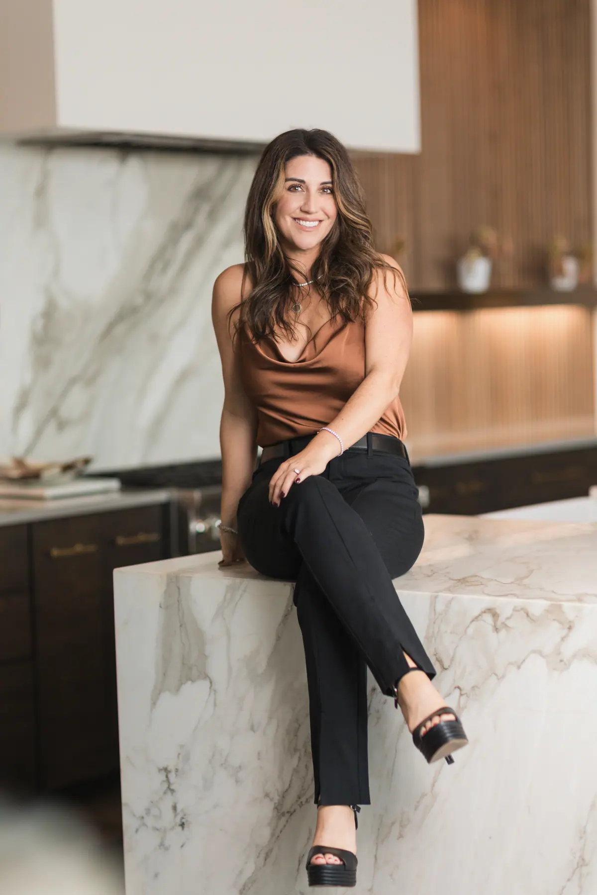 Cynthia Mattiza smiling, seated on a marble kitchen island in a modern luxury home