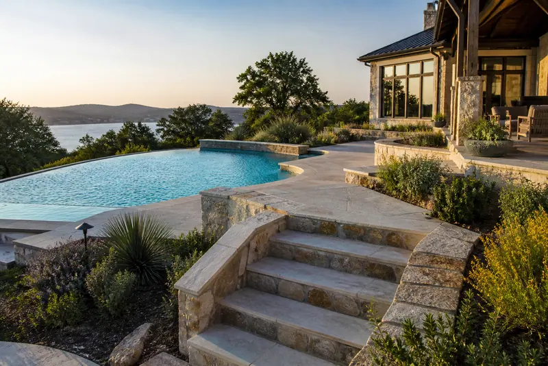 Infinity pool and limestone steps overlooking a lake at sunset